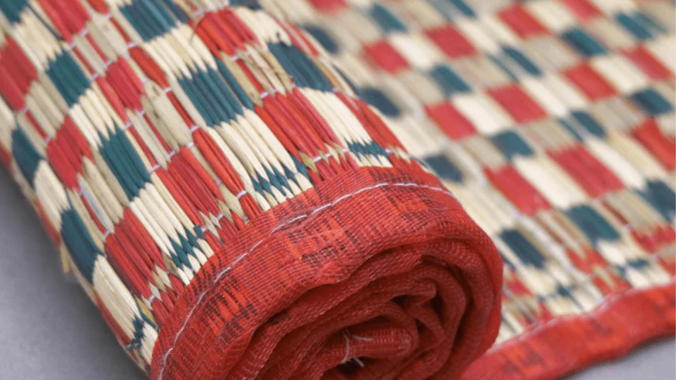 Rolled woven mat with red, blue, and beige geometric pattern and stitched red border close-up