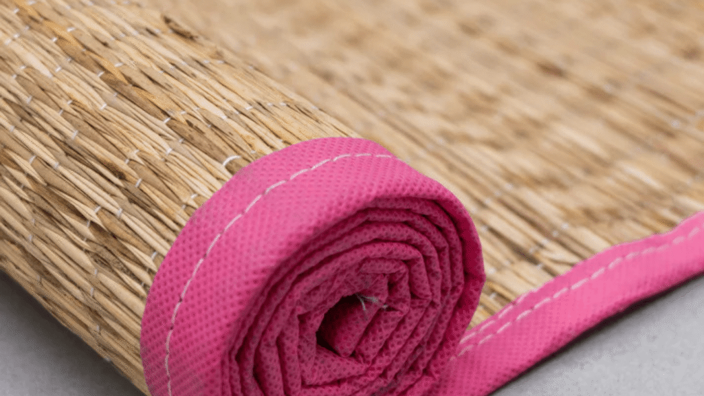 Rolled natural straw mat with pink fabric edge and stitching detail on a smooth surface